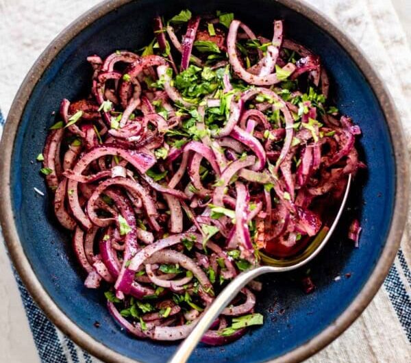 Bowl of bright pink sumac onions with parsley ready to serve