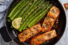 Golden lemon butter salmon with asparagus on a sheet pan garnished with fresh lemon slices and herbs